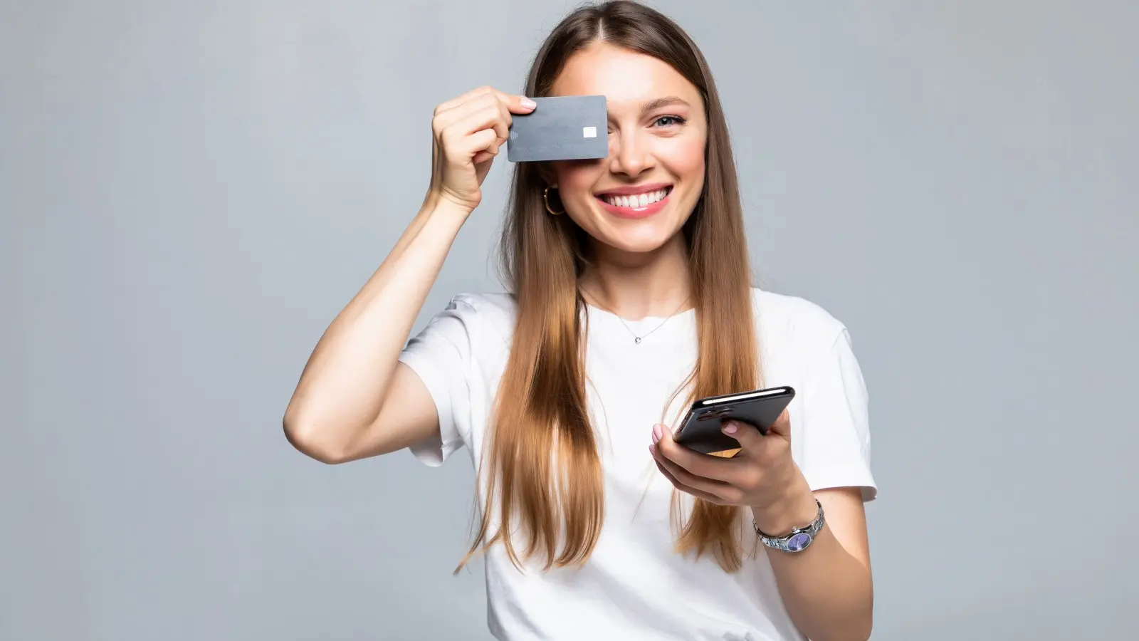 Mujer sonriente sosteniendo tarjeta de crédito y teléfono. ¿Qué requisitos necesitas para obtener un préstamo hipotecario?